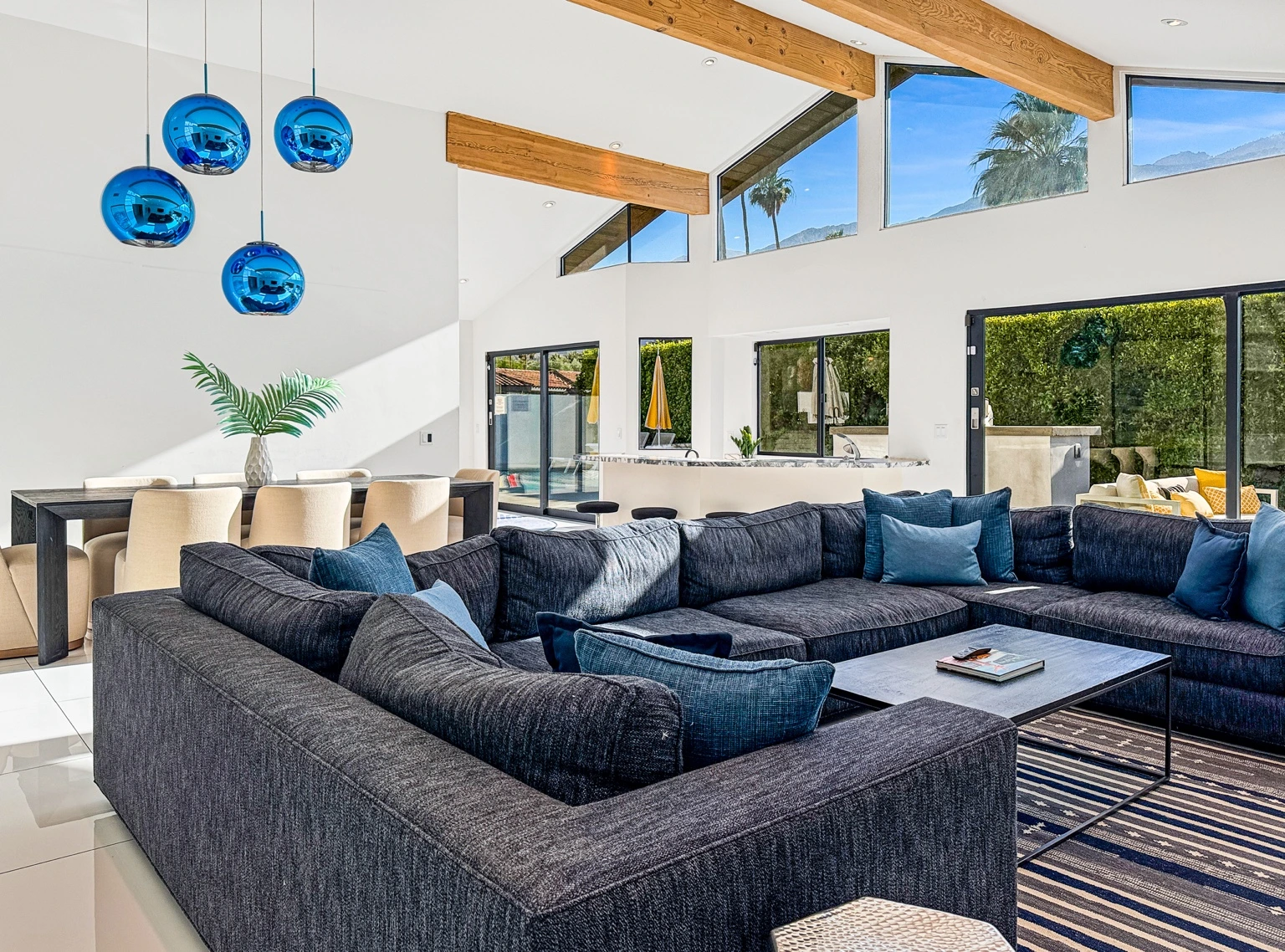 Bright living and dining space with blue pendant lights, exposed wood beams, and mountain views